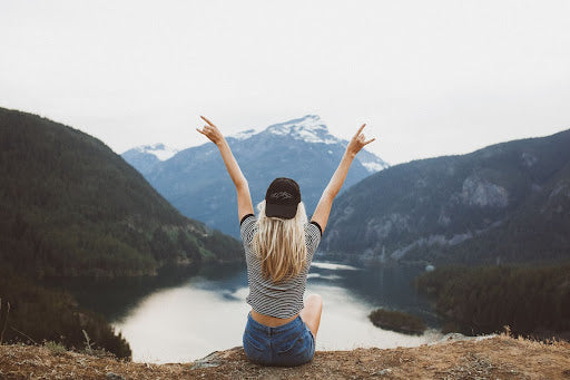 Women doing the rock-on-hand gesture after a hike, overlooking mountains and water